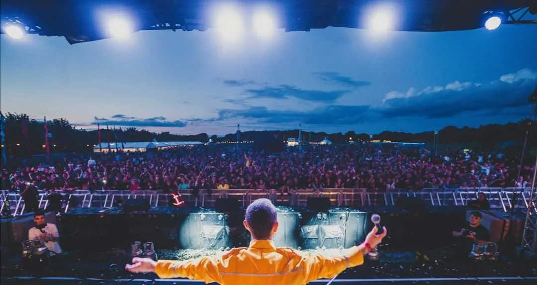 Eddie Devlin as Freddie Mercury, arms out to a packed festival crowd
