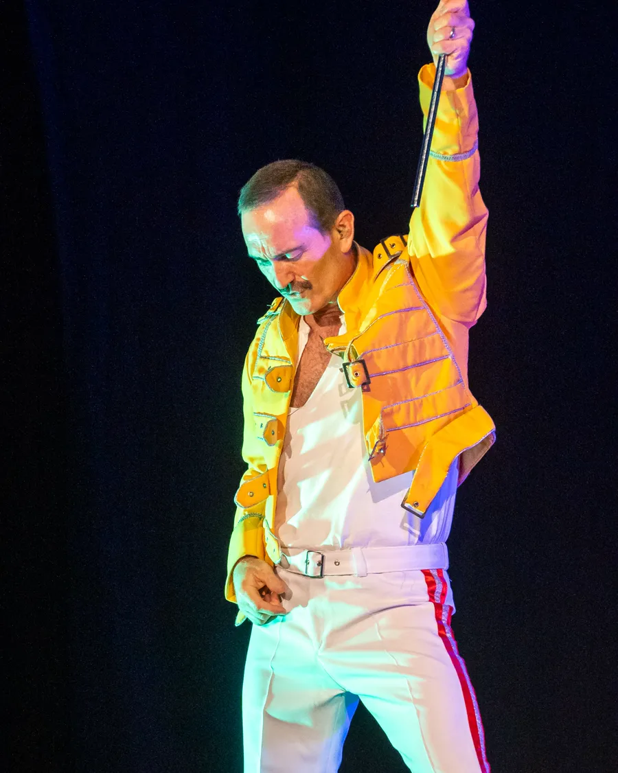 Eddie Devlin as Freddie Mercury in the yellow buckled jacket, mic stand held high